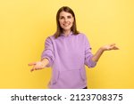 Small photo of Openhearted generous woman outstretching hands looking at camera with kind smile, greeting and regaling, happy glad to see you, wearing purple hoodie. Indoor studio shot isolated on yellow background.