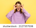 Portrait of happy smiling woman covering eyes with gold bitcoin, blockchain concept, cryptocurrency, digital money, wearing purple hoodie. Indoor studio shot isolated on yellow background.