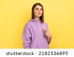 Small photo of This is me. Egoistic haughty woman pointing herself and looking at camera with arrogance, superiority, proud of achieved goal, wearing purple hoodie. Indoor studio shot isolated on yellow background.