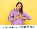 Small photo of Portrait of overworked depressed woman frowning suffering sudden heart attack, myocardial infarction, risk of breast cancer, wearing purple hoodie. Indoor studio shot isolated on yellow background.