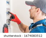Professional Electric Technician Installing Main Fuses Box Inside Newly Developed House. Residential Electrical System. Industrial Theme.