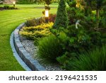 Landscaped Garden at the Backyard with Evenly Mowed Lawn and Island Bed with a Variety of Shrubs, Bushes, Trees and Evergreen Plants. Decorated with Bollard Outdoor Lighting Lamp.