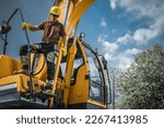 Small photo of Professional Heavy Duty Machinery Operator Standing on Excavator Machine. Construction Industry Theme.