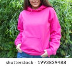 Small photo of The smiling woman is wearing a pink hoodie, facing the camera outside. There is a blank space on the hoodie for a logo, design or text that may allude to a breast cancer awareness campaign.