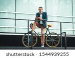Casual handsome middle-aged businessman is going to the office by bicycle. He is sitting on the bike and using smart phone.