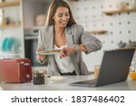 Shot of a multi-tasking young business woman having a breakfast and using laptop in her kitchen while getting ready to go to work.