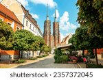 Street with cobblestone road with green trees, colorful buildings, summer cafe, Cathedral of St. John the Baptist church with two spires in old historical city centre, Ostrow Tumski, Wroclaw, Poland