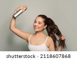Beautiful young woman applying hair spray on her hair.