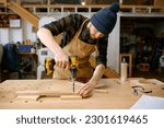 Small photo of Young man jointer working with drill leaning over table at carpentry workshop