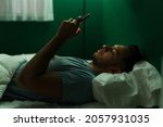 Handsome latin man texting on his smartphone and checking social media before falling asleep at night