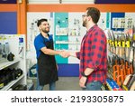 Cheerful male employee smiling shaking hands with a young man and greeting him to the hardware store during his shopping