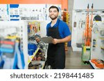 Cheerful retail worker with a blue uniform smiling holding a clipboard for inventory and looking happy to work at the hardware store 