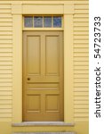Small photo of An unadorned yellow door set in to the facade of a wooden building. Vertical shot.