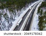 Small photo of white trucks on the higthway. convoy whith cargo driving by road seen from the air. Top view landscape. shooting from a drone. Cargo delivery in winter. Aerial view of snow road in winter forest