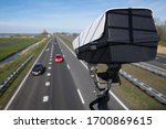 Security CCTV camera or surveillance system observes vehicular traffic on a road in the Netherlands with intentional blur on background