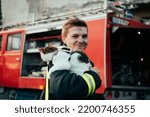 Small photo of Close-up portrait of heroic fireman in protective suit and red helmet holds saved cat in his arms. Firefighter in fire fighting operation.