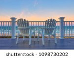 Empty Adirondack chair on a deck balcony overlooking the beach and the ocean at sunset