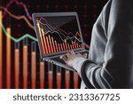 Small photo of Close up of hand holding and using laptop with downward red crisis chart grid on blurry dark background. Recession and economic fall concept