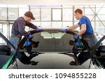 Automobile special workers replacing windscreen or windshield of a car in auto service station garage. Background
