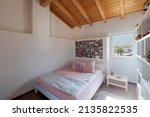 A girl's bedroom with white walls, a double bed and a windows's views on nature. Exposed wooden beams. Nobody inside