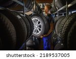 Hardworking experienced worker holding tire and he wants to change it In the tire store. Selective focus on tire.