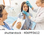 Beautiful young woman is sitting with closed eyes in doctors office, two doctors are examining her face and making notes