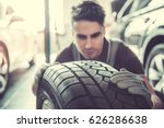 Handsome young auto mechanic in uniform is examining a tire while working in auto service