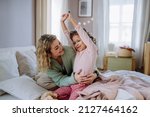 Happy mother hodling her little daughter stretching in bed when waking up in morning.