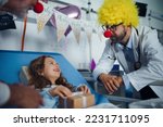 Small photo of Happy doctor with clown red noses celebrating birthday with little girl in hospital room.