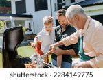 Small photo of Multi generation family grilling outside on backyard in summer during garden party