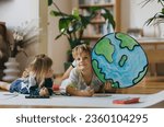 Small photo of Siblings lying on stomach and painting at home with watercolors, markers and tempera paints, creating a model of planet Earth.
