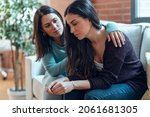 Shot of pretty young woman supporting and comforting her sad friend while sitting on the sofa at home.