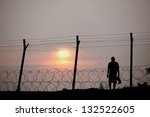 Small photo of Silhouette of a prisoner behind a barbed wire fence in a concentration camp against fiery setting sun.