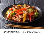Asian food: teriyaki beef with red and yellow bell peppers, broccoli and sesame seeds close-up on a plate on a black table. horizontal