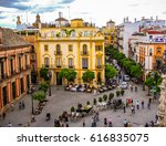 Small photo of SEVILLE, SPAIN - May 7, 2011: Tourists and locals mill around the Plaza Del Triunfo in Seville, Spain with rooftops and the Santa Cruz church in the distance.