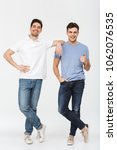 Small photo of Full length photo of two handsome men pals 30s wearing casual t-shirt and jeans smiling and posing together on camera with thumb up isolated over white background