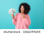 Portrait of american successful woman 20s with afro hairstyle holding lots of money dollar ï»¿banknotes isolated over blue background