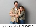 Portrait of a cheerful young couple standing together isolated over gray background, hugging