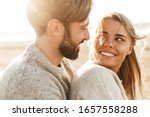 Close up of a smiling beautiful young couple embracing while standing at the beach
