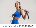 Young white fitness woman in sportswear with ponytail standing over white wall background, holding skipping rope