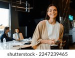 Hispanic young woman smiling and using cellphone during offline meeting in office