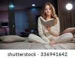Beautiful young curly woman in pajamas sitting on the bed and reading
