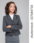 Small photo of Smug priggish assured successful young curly business woman in gray suit with arms crossed
