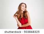 Portrait of a cheerful young brunette woman in red santa claus dress posing and looking away over white background