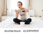 Cute pregnant young woman with remote control eating ice cream and watching TV at home