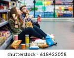Portrait of a young funny hungry couple sitting on the supermarket floor and eating junk food