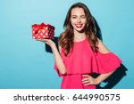 Portrait of a happy smiling girl in dress holding present box and winking isolated over blue background
