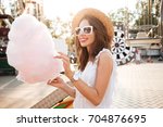Portrait of a smiling pretty girl in sunglasses holding cotton candy at amusement park