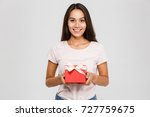 Portrait of a happy pretty asian woman holding present box while standing and looking at camera isolated over white background
