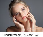 Attractive young girl touching her lips. Photo of blonde girl with perfect skin on grey background. Beauty & Skin care concept